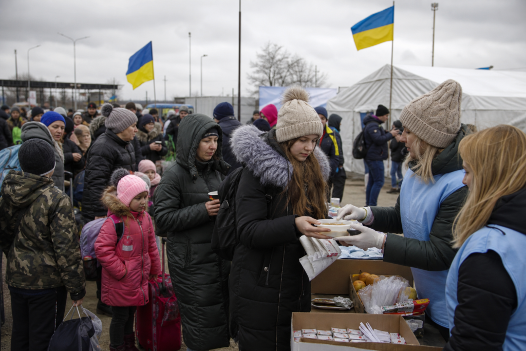 Змучені та голодні біженці біля прикордонного пункту, волонтери роздають їжу та допомогу